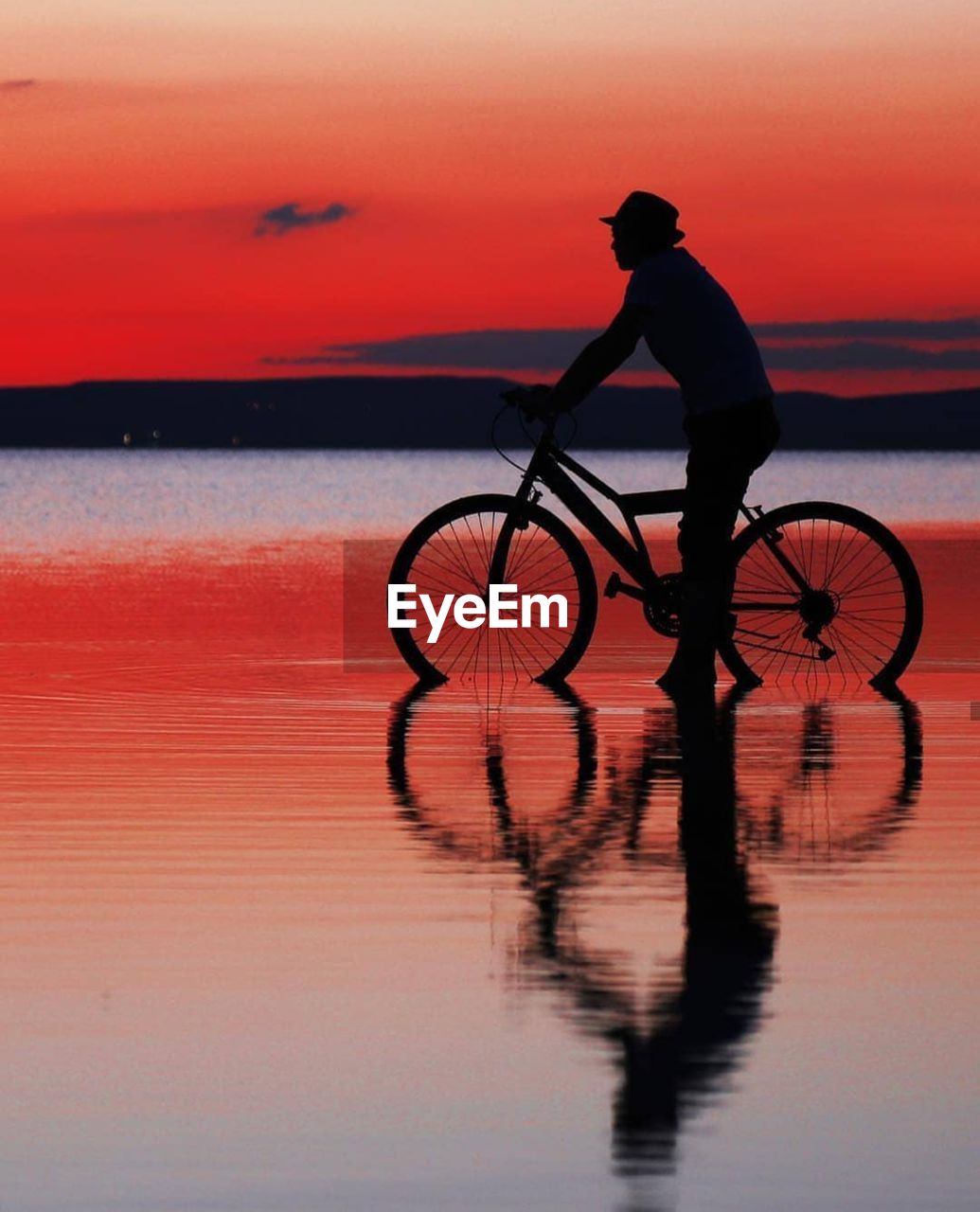 Silhouette man riding bicycle at sea against sky during sunset
