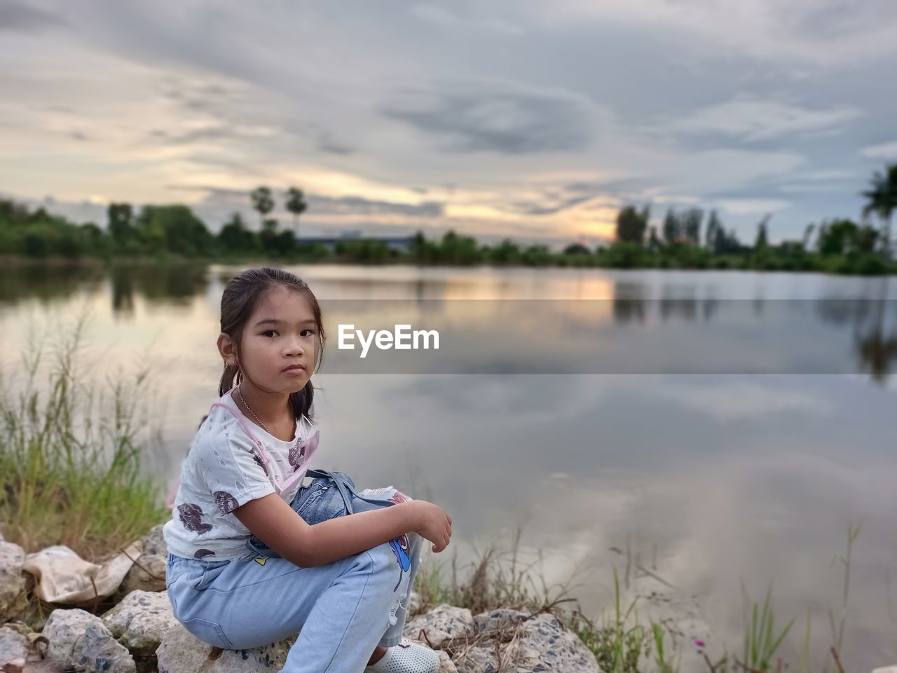 Portrait of girl sitting on lake against sky