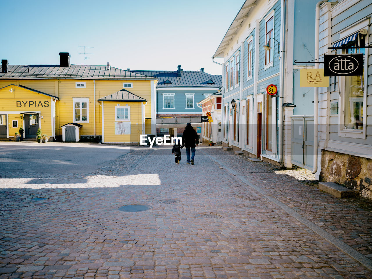 REAR VIEW OF MAN WALKING ON FOOTPATH AMIDST BUILDINGS IN CITY