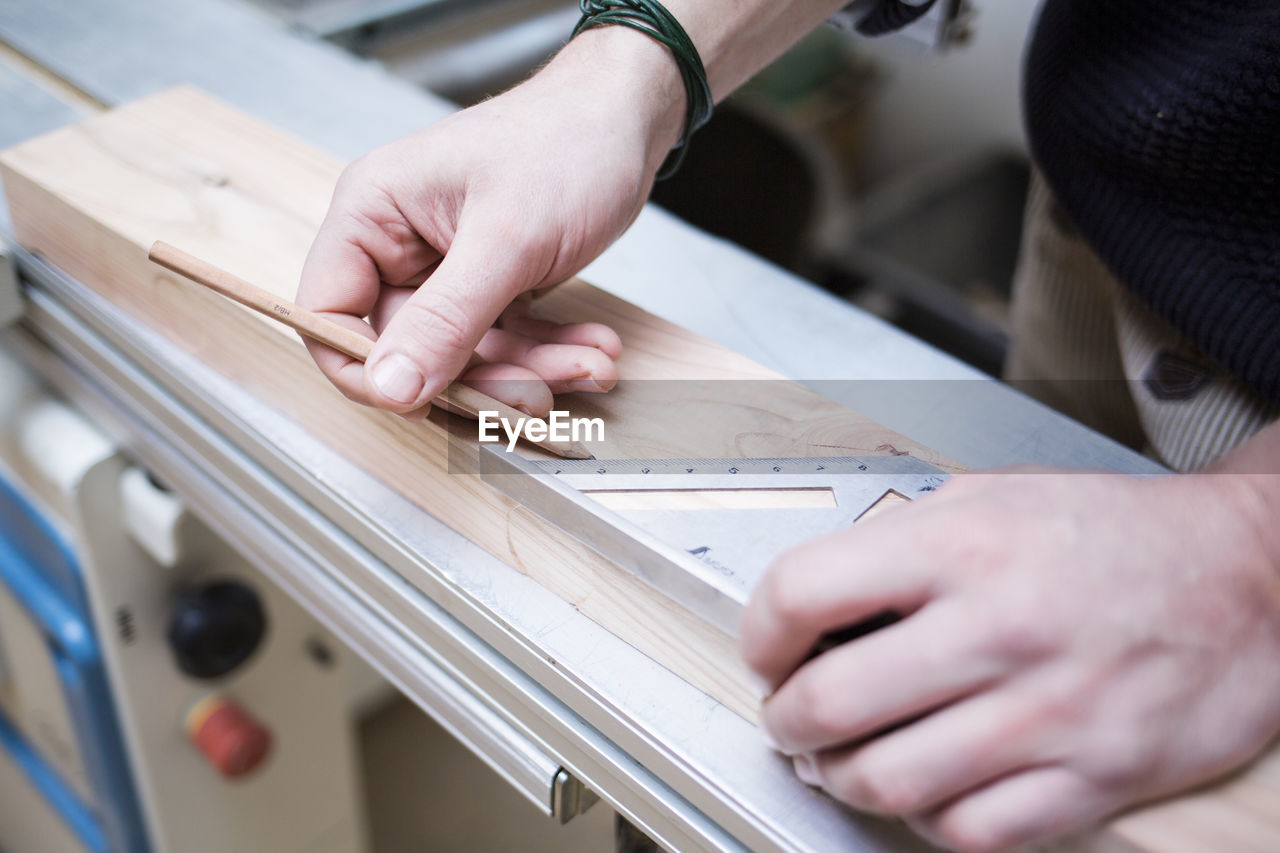 Cropped hands of carpenter measuring wooden planks at workshop