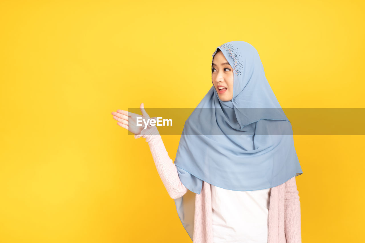 WOMAN STANDING AGAINST YELLOW COLORED BACKGROUND