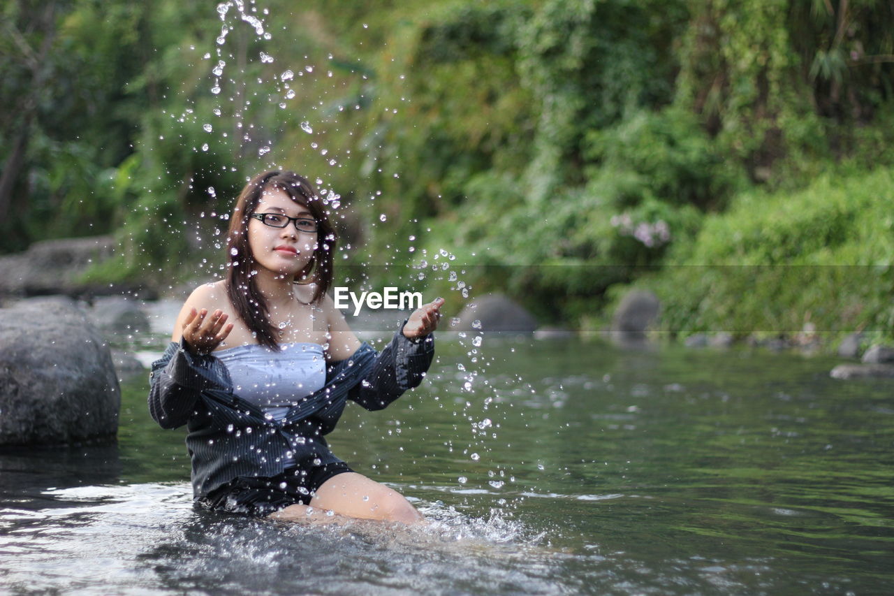 Portrait of young woman splashing water in lake