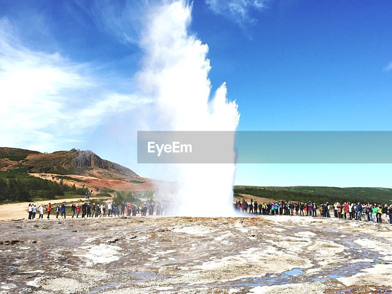 Tourists watching geyser against sky