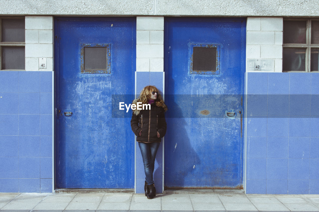 Portrait of woman standing against door of building