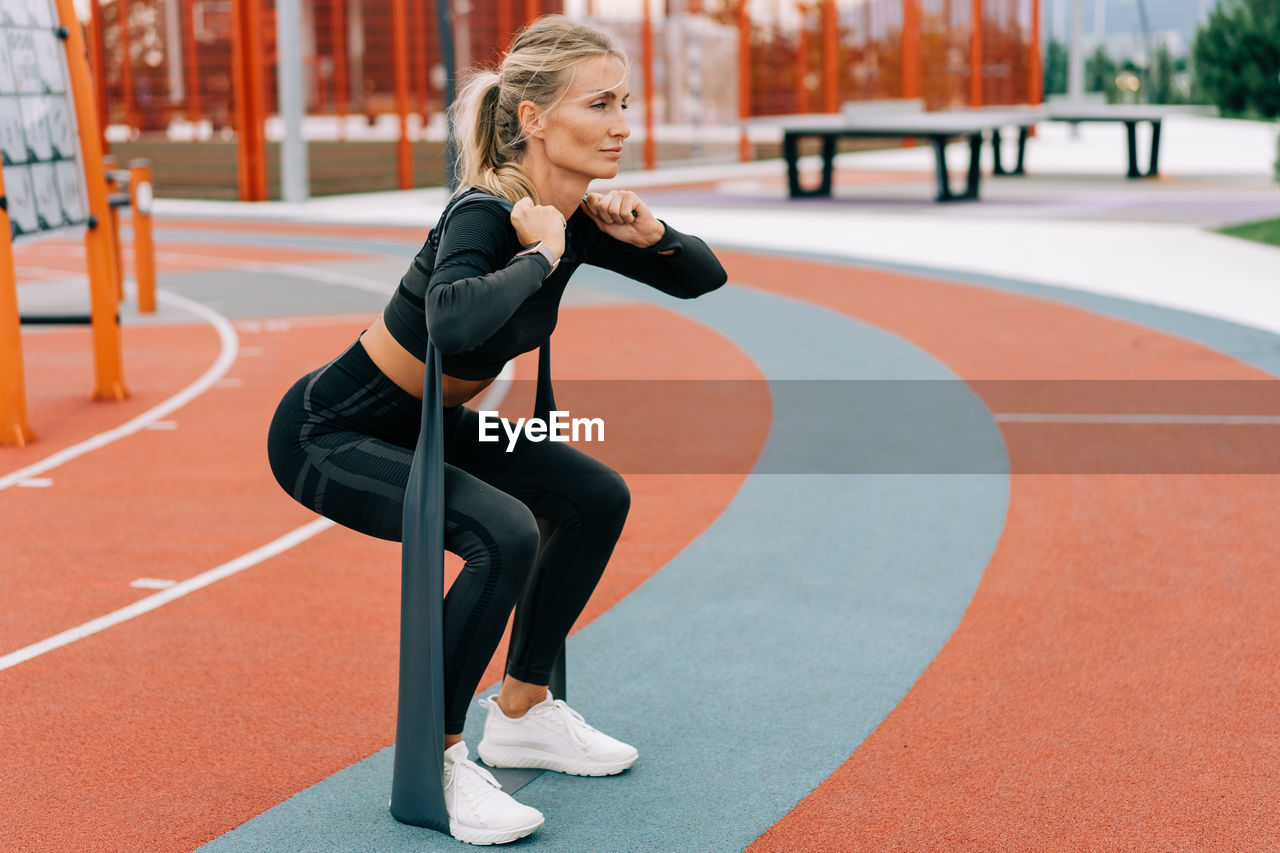 Young athletic woman is training on the sports ground using sports elastic bands.