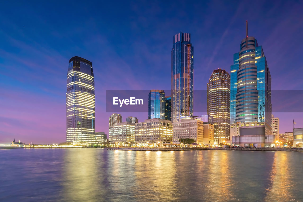 Illuminated modern buildings in city against sky at night