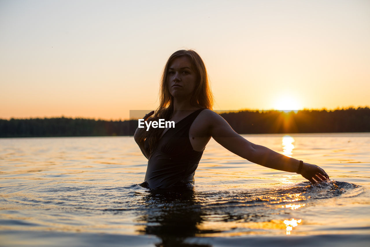 Beautiful russian girl in a long black swimsuit swims outside the city on the lake.