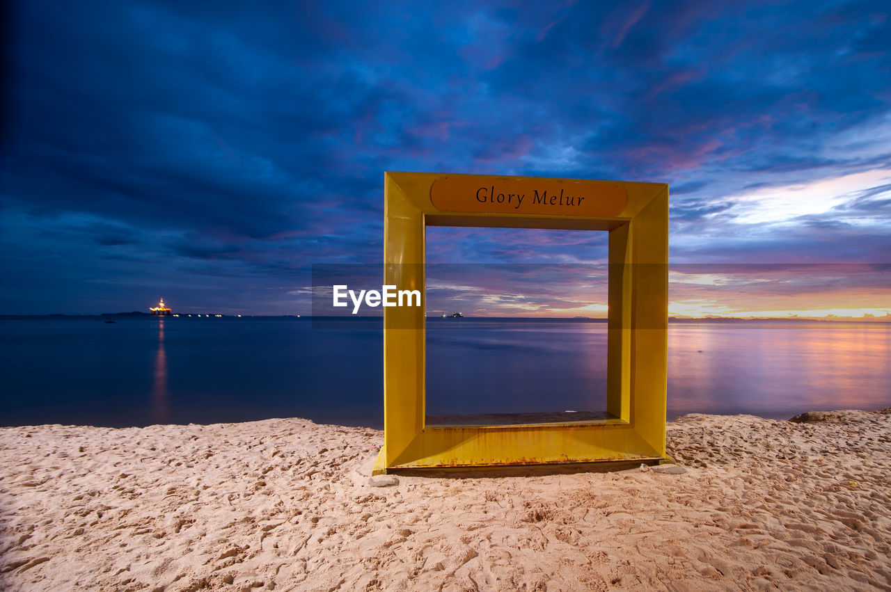 sky, cloud, sea, beach, land, water, horizon, nature, sunset, ocean, scenics - nature, sand, sunlight, beauty in nature, communication, dramatic sky, horizon over water, dusk, blue, landscape, tranquility, travel destinations, no people, tranquil scene, seascape, travel, architecture, environment, cloudscape, yellow, outdoors, coastline, evening, vacation, sign, trip, holiday, coast, urban skyline, text, sun, summer, idyllic