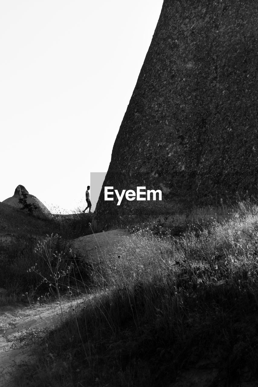 Man walking by rock formation against clear sky