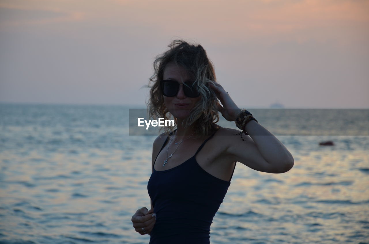 Young woman standing at beach against sky during sunset