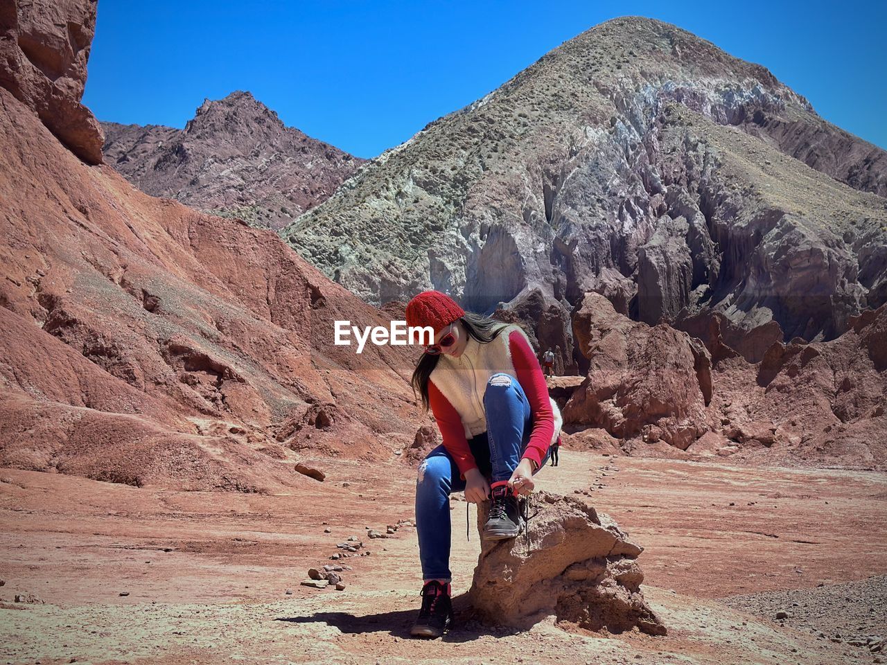 Front view of woman sitting on rock against clear sky