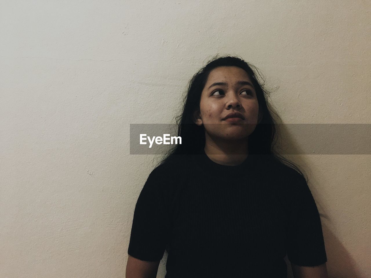 Young woman looking away while standing against wall