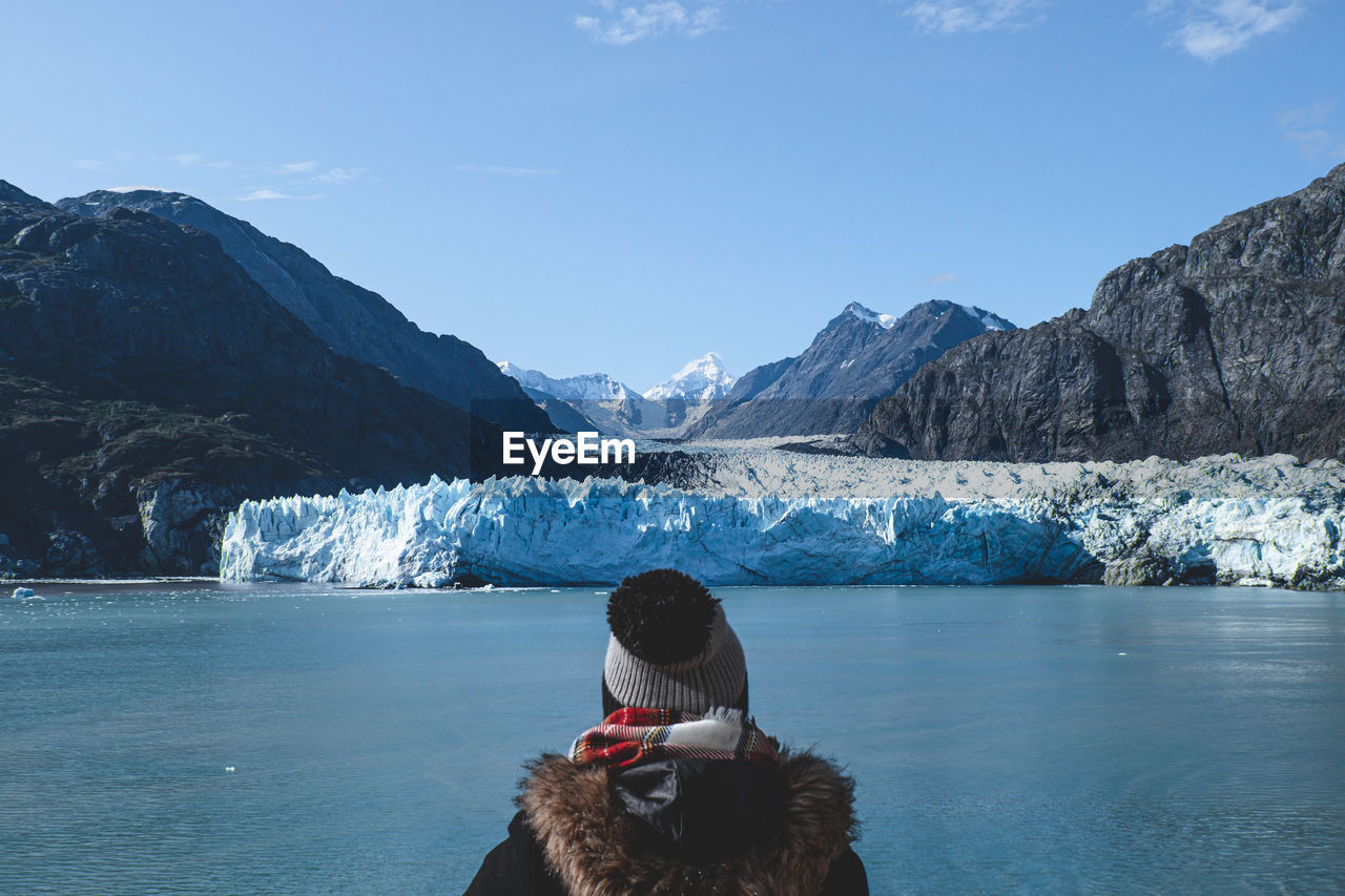 Rear view of woman looking at glacier while standing by sea