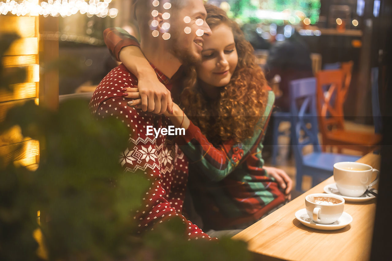 Loving couple in a cafe hug and drink cocoa. photo from the street. reflection of lights 