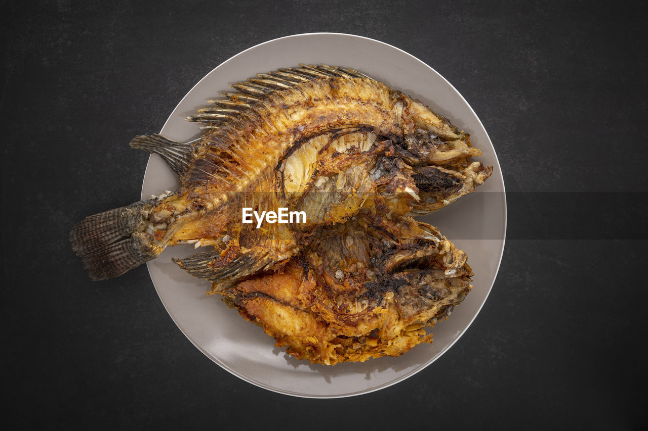 Tasty large fried nile tilapia fish in ceramic plate on dark tone texture background, top view