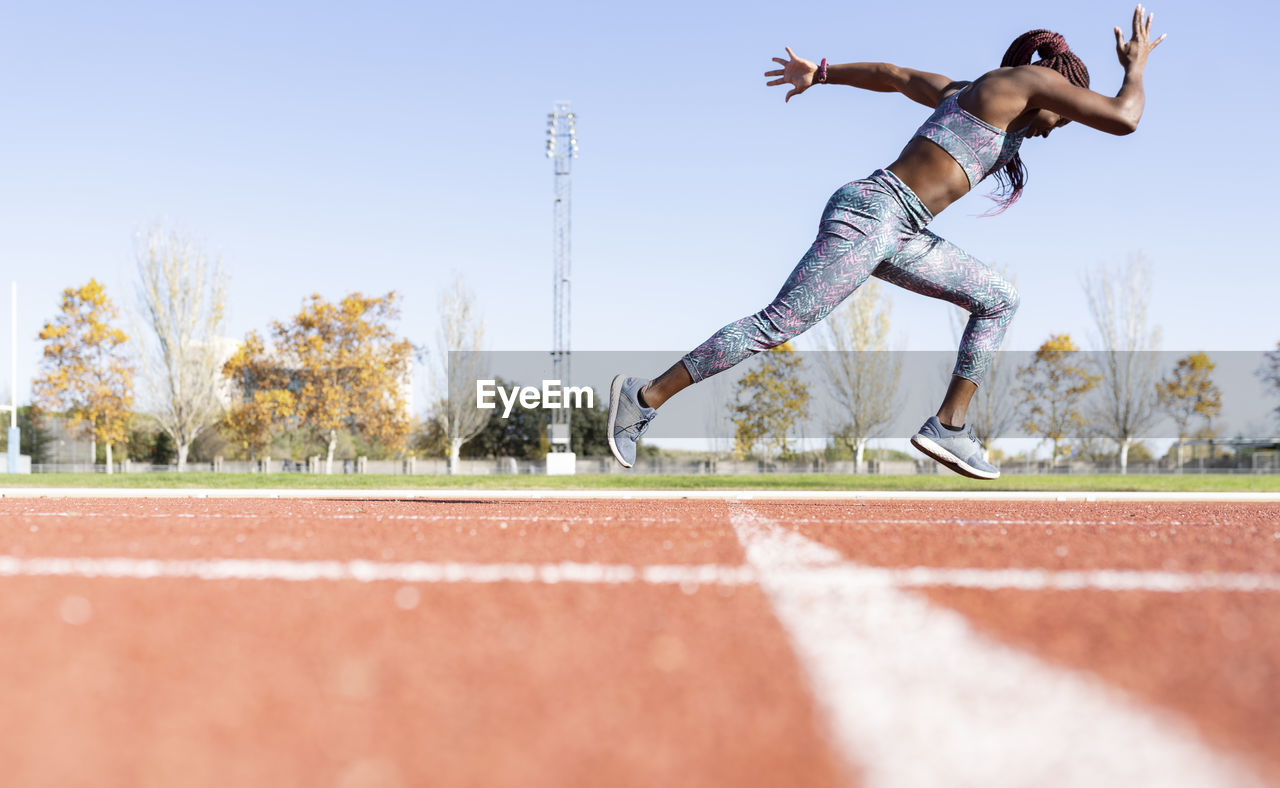 Sportswoman with dedication running on sports track against clear sky during sunny day