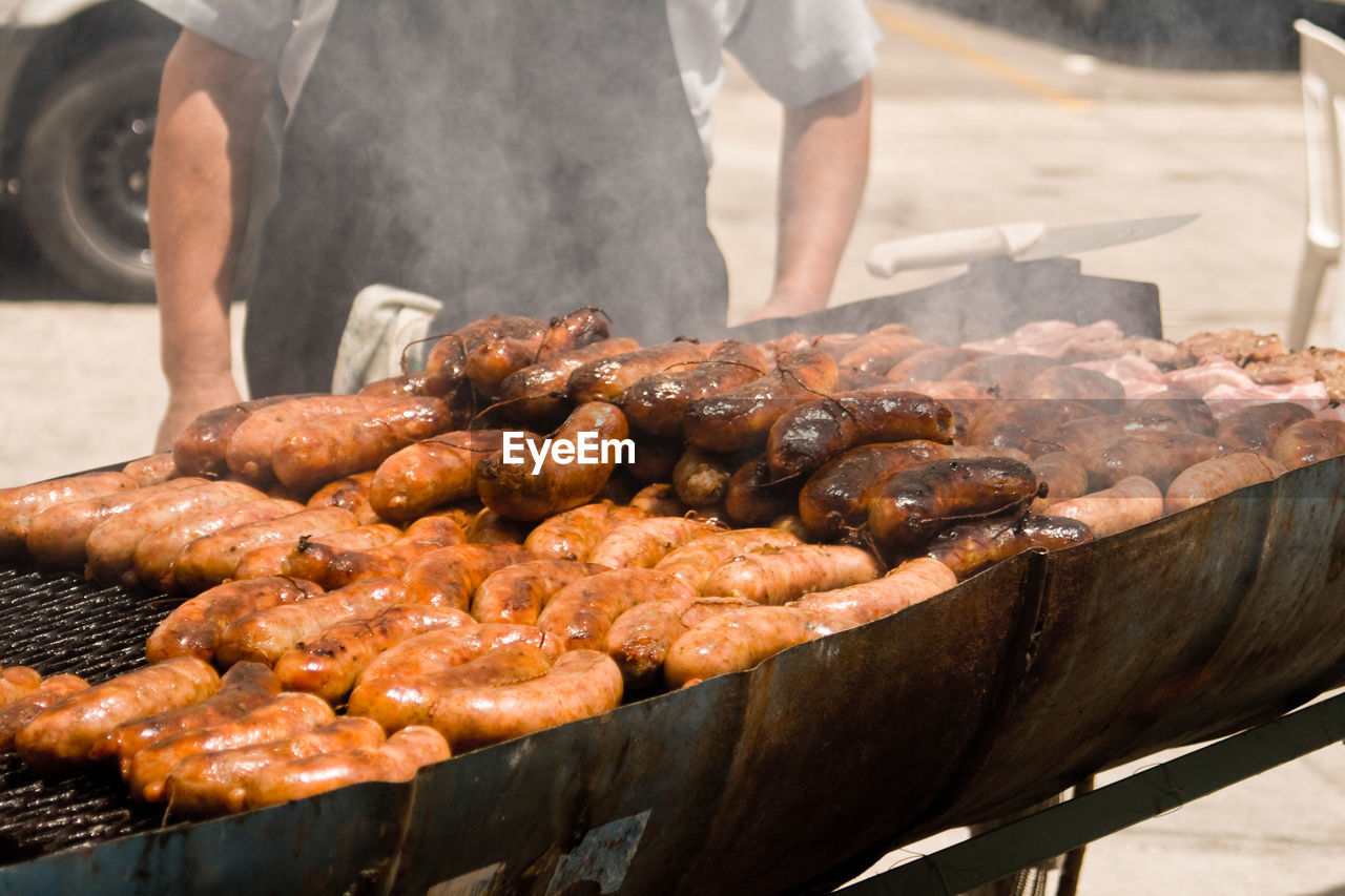 Midsection of man cooking chorizos on barbecue in city