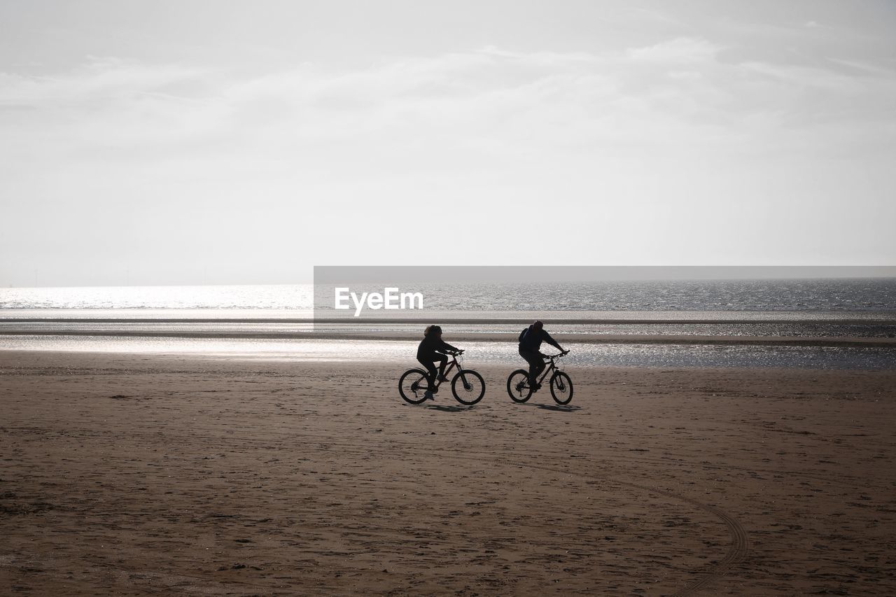 PEOPLE RIDING BICYCLE ON BEACH