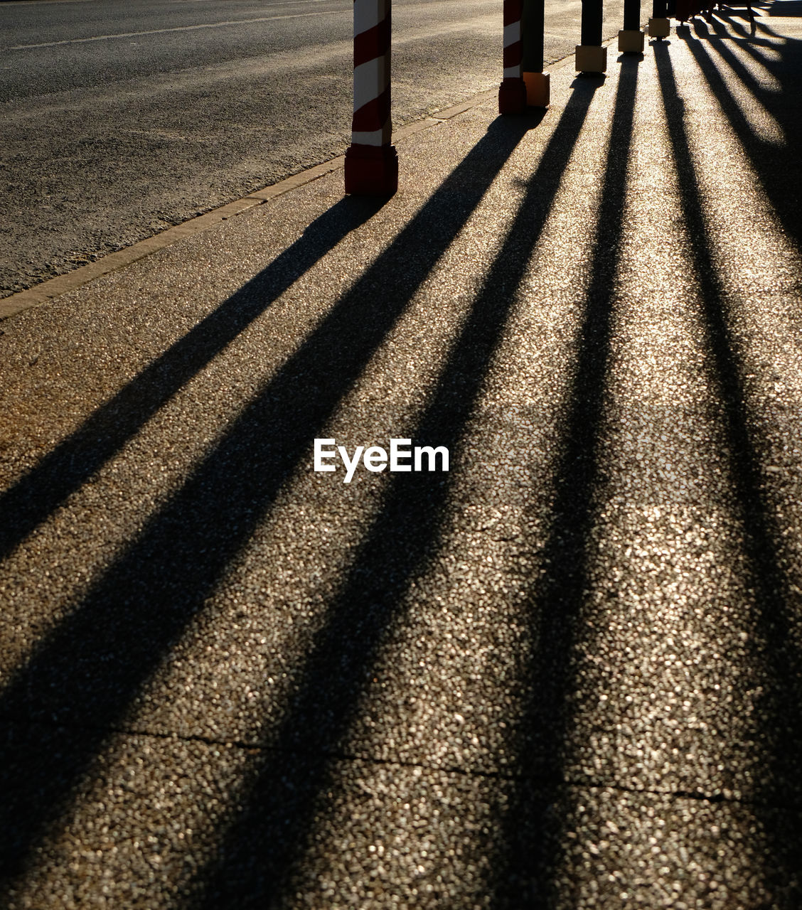 Shadow of bollards on sidewalk in city during sunset