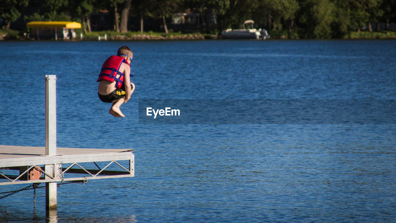 Boy jumping on lake during sunny day