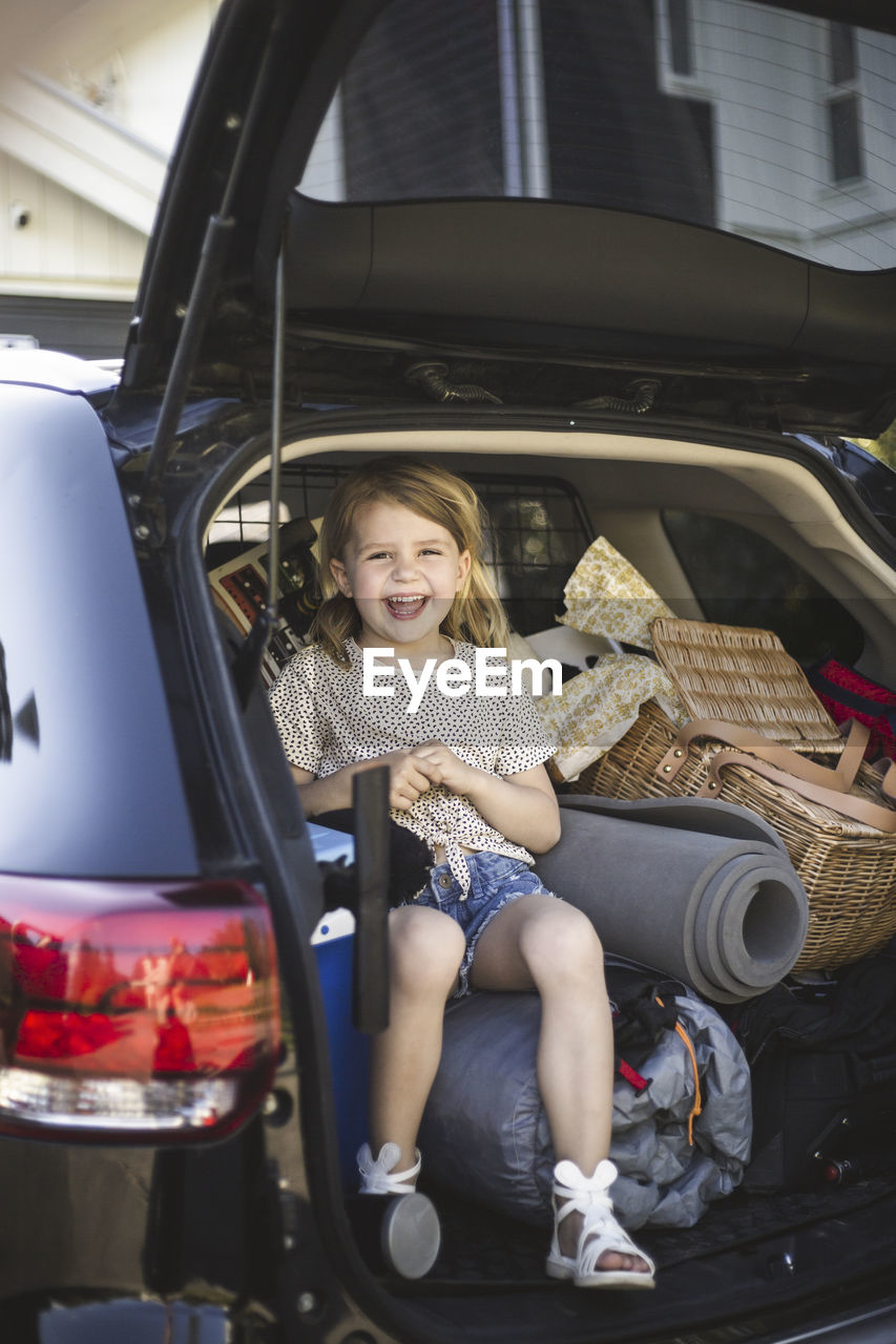 Portrait of mother, father and two daughters standing by car at electric vehicle charging station