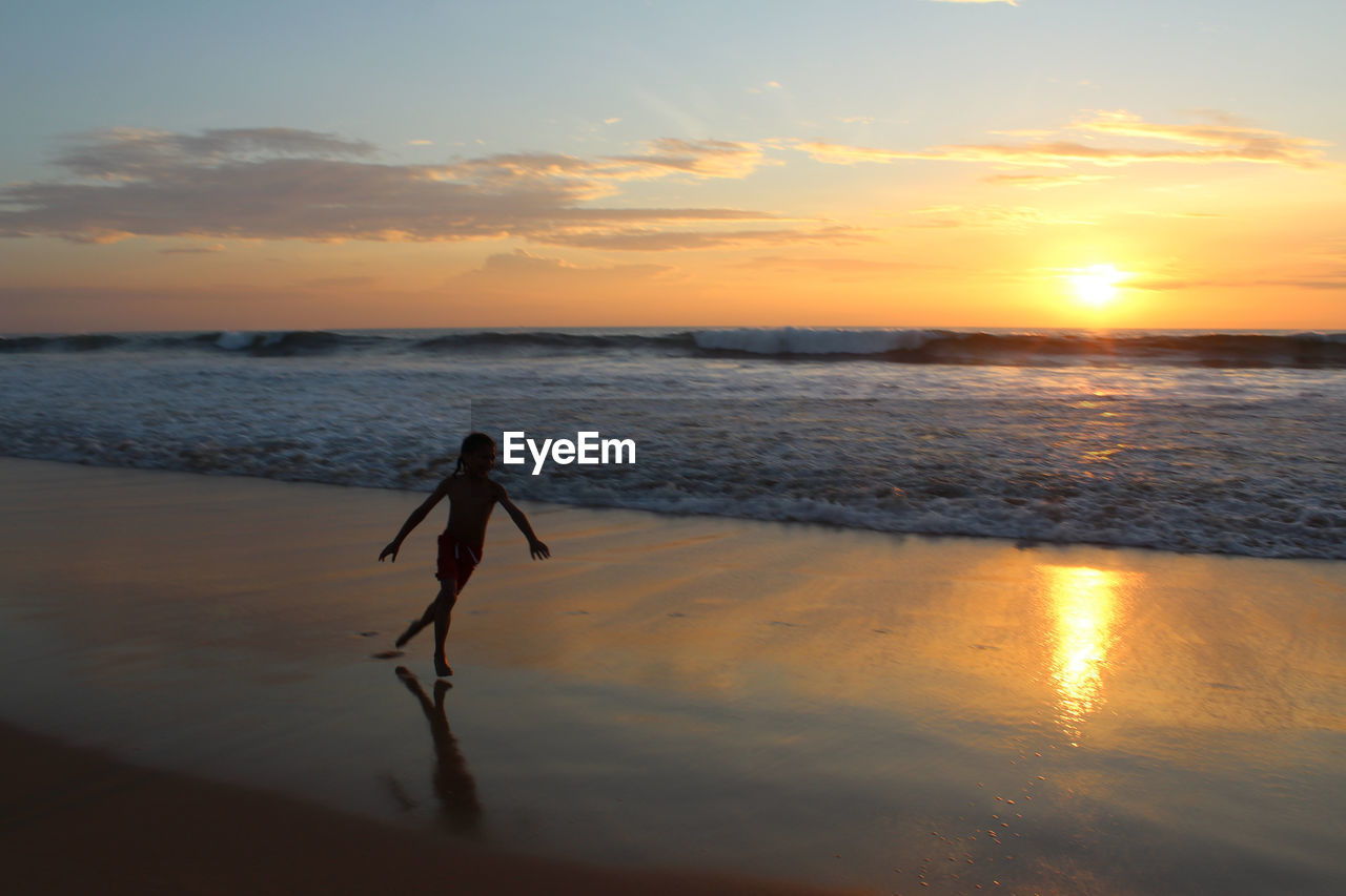 Boy running at beach against sky during sunset