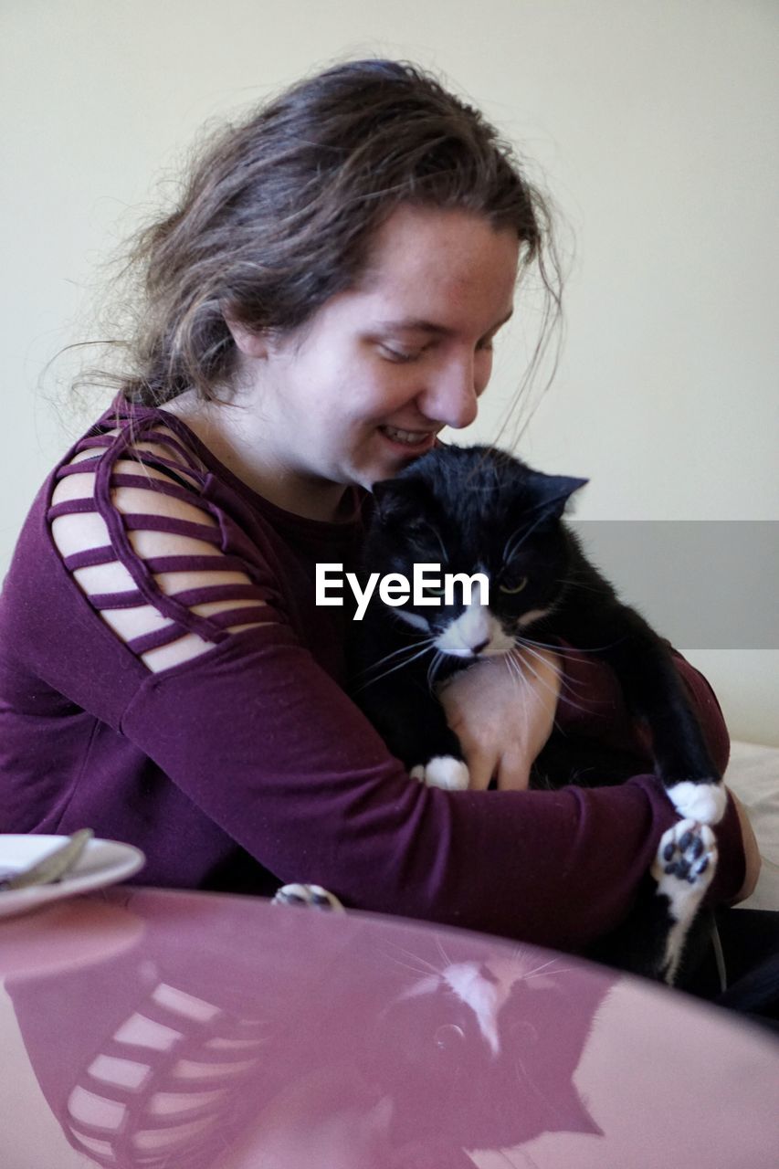 Smiling teenage girl holding cat while sitting at home
