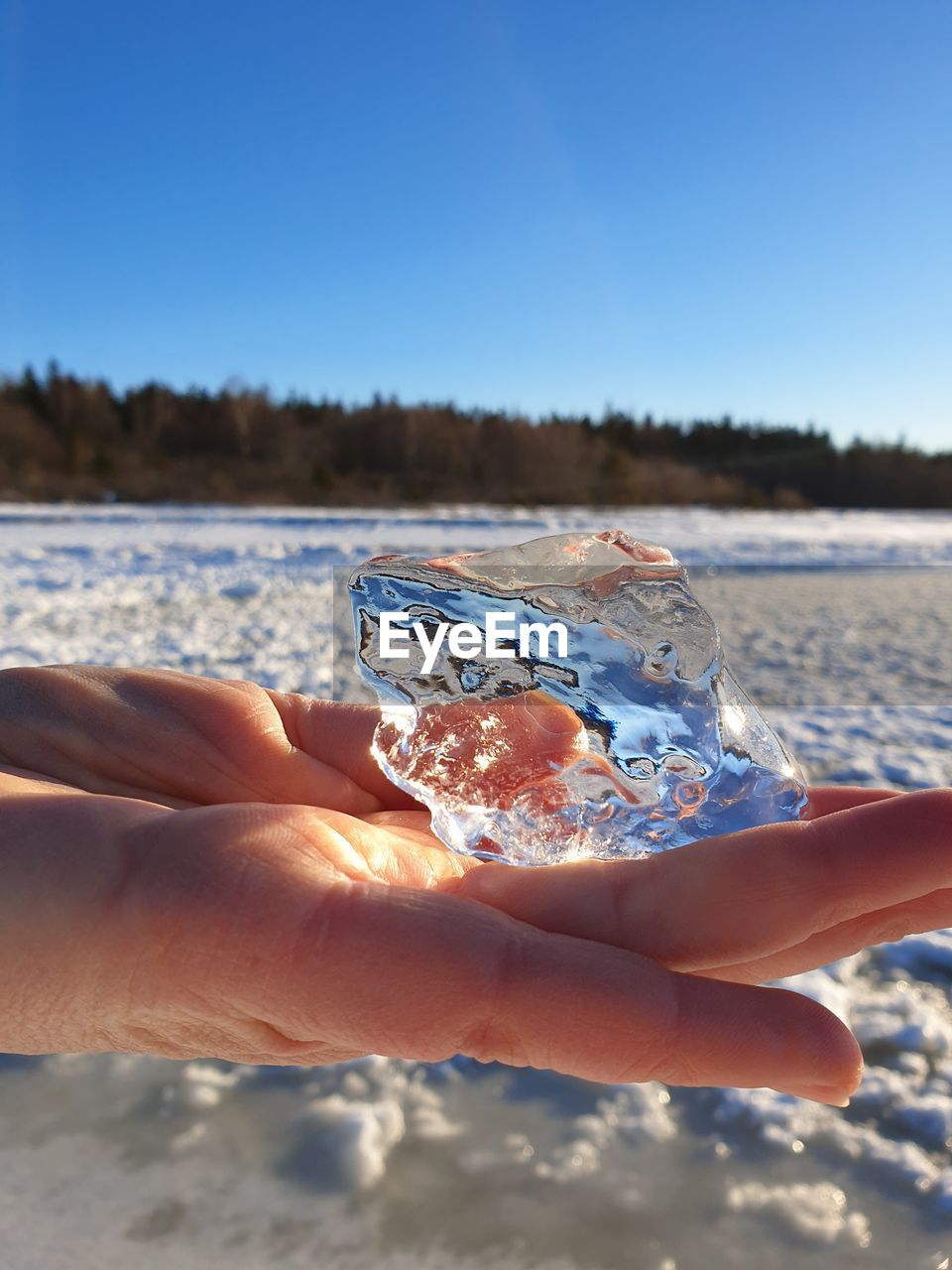 Cropped hand of person holding ice against clear sky during winter