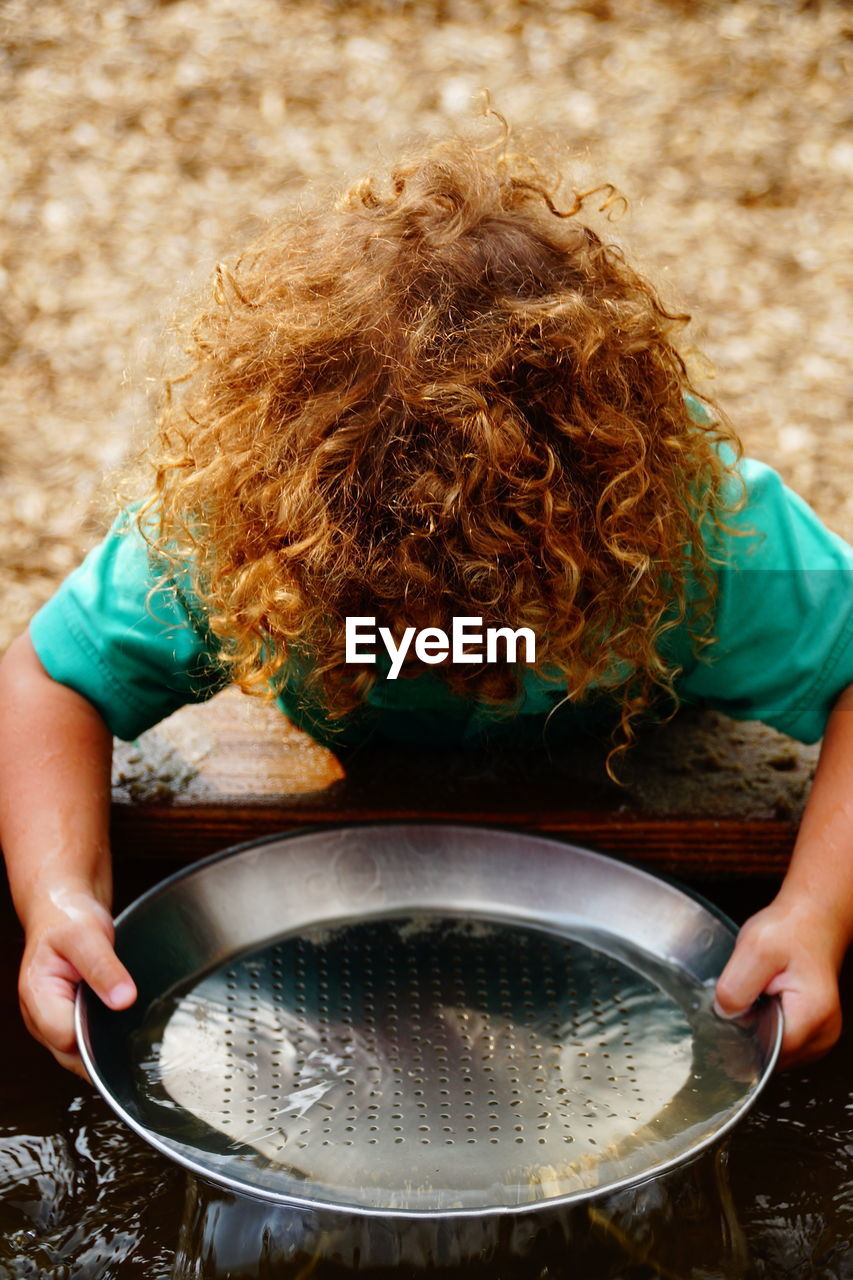 High angle view of boy with blond curly hair washing plate in trough