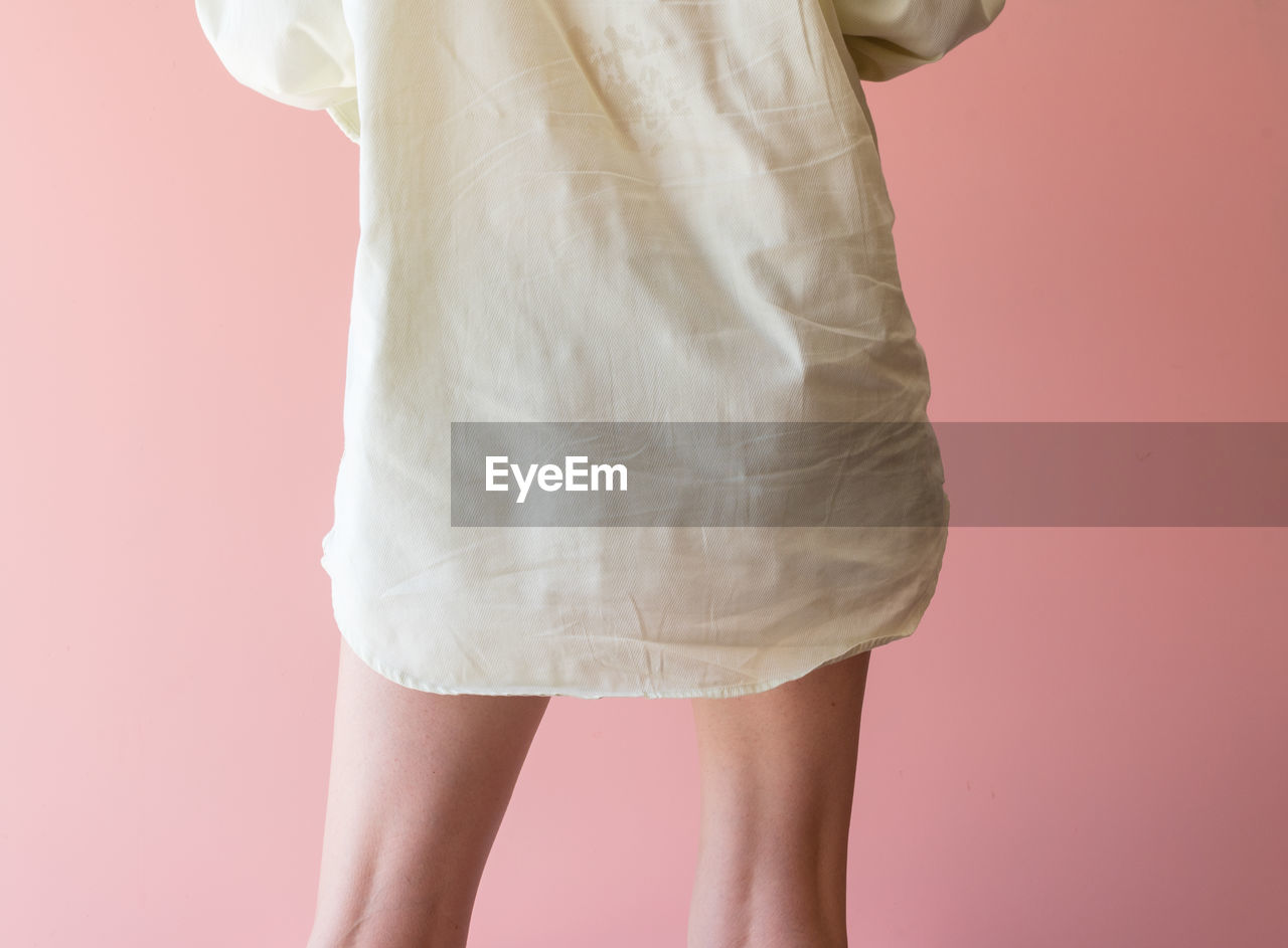 Rear midsection of mature woman standing against colored background