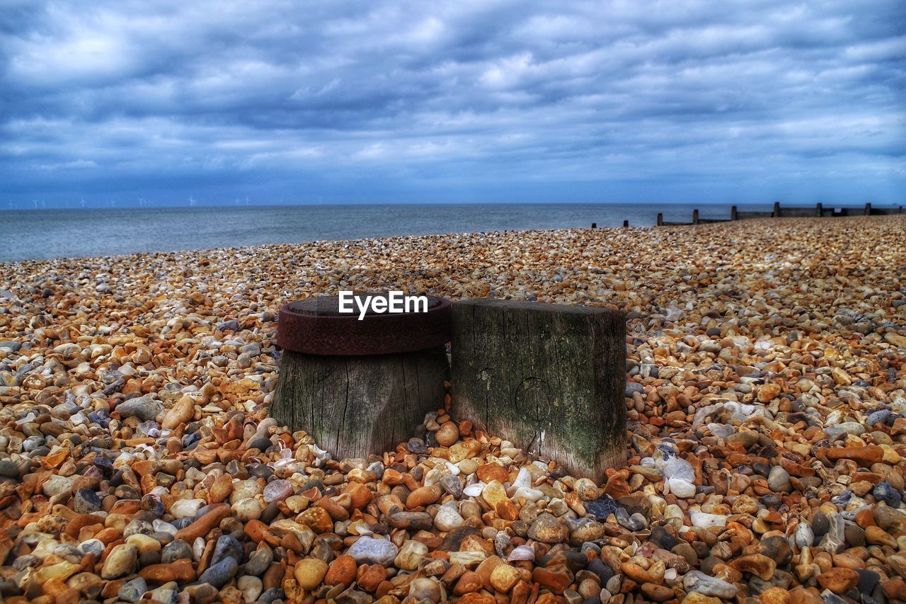 VIEW OF PEBBLES ON BEACH AGAINST CLOUDY SKY