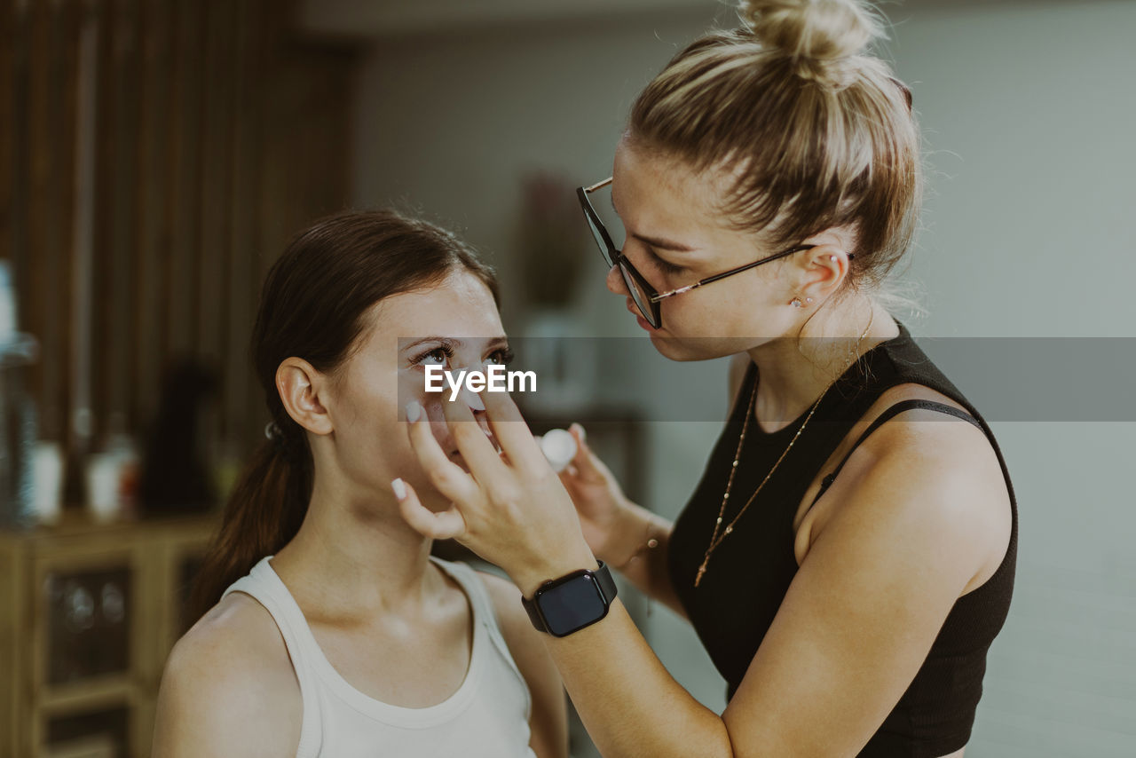 A young makeup artist applies a medicinal liquid under a girl s eyes.