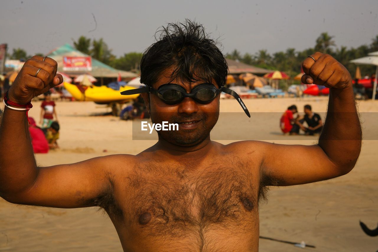 PORTRAIT OF YOUNG MAN WITH SUNGLASSES AT BEACH