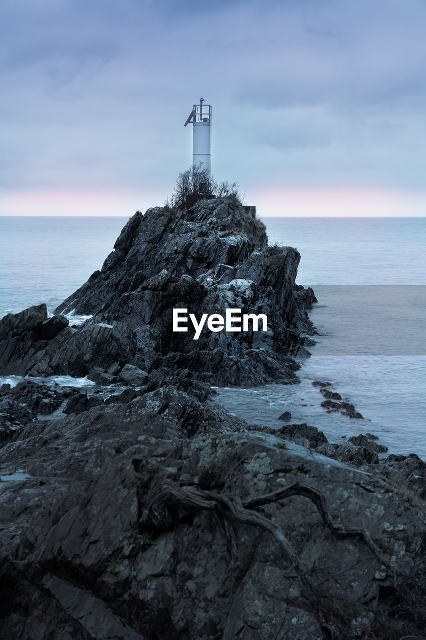 Lighthouse on rock by sea against sky