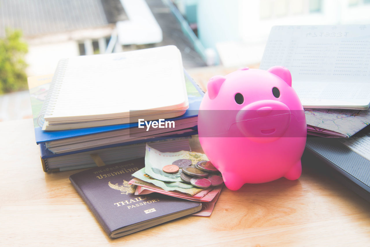 High angle view of money with piggybank and passport by books on table