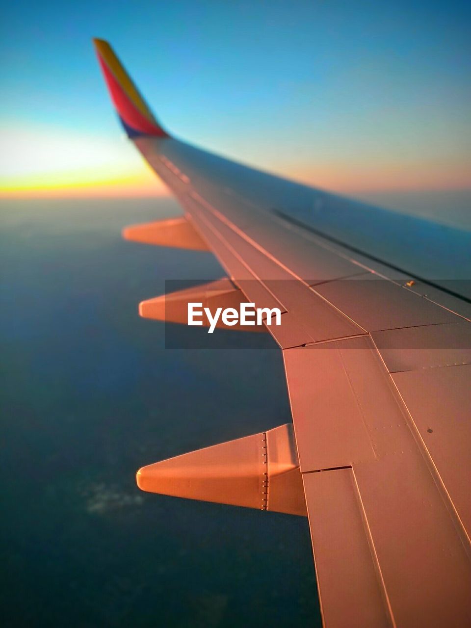 Cropped image airplane wing flying against sky during sunset