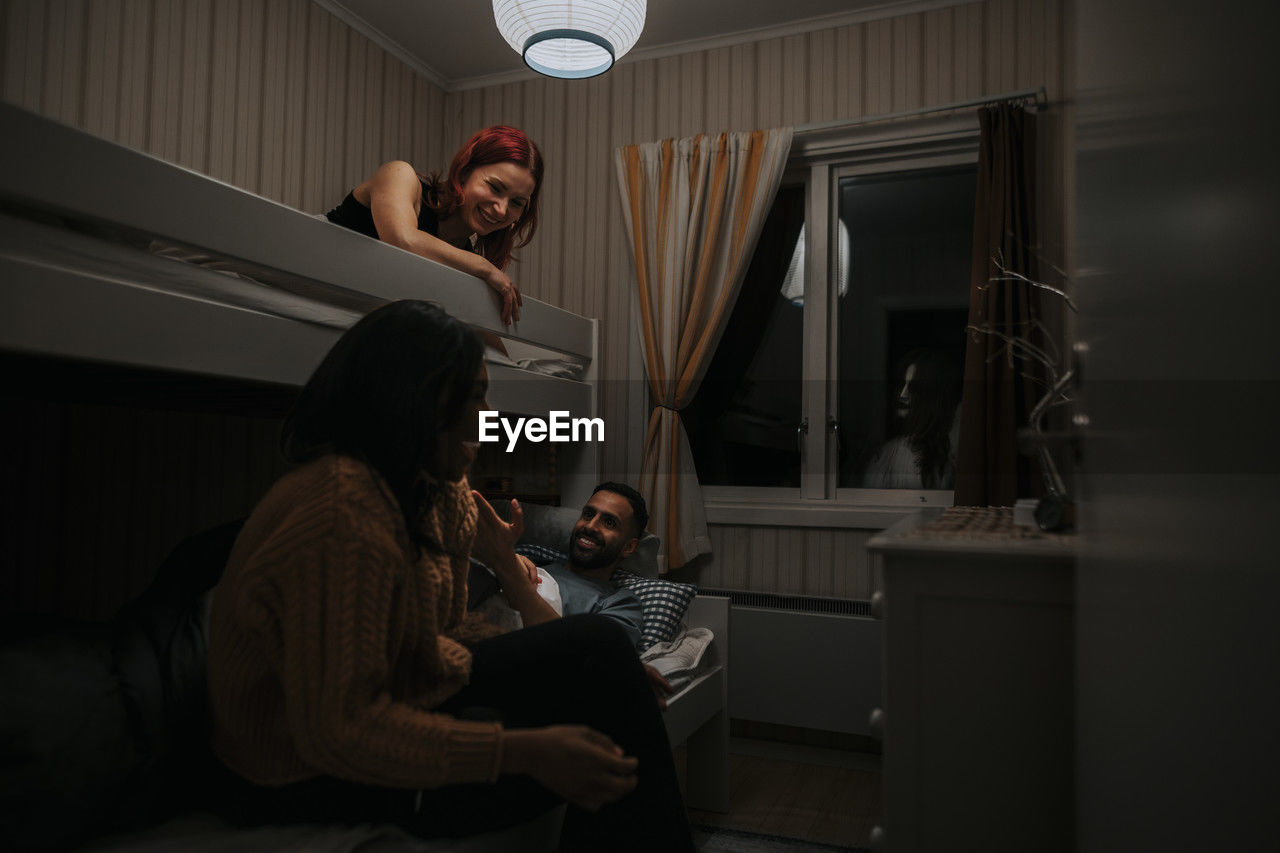 Multiracial friends having fun in cabin while ghost looking through window at night