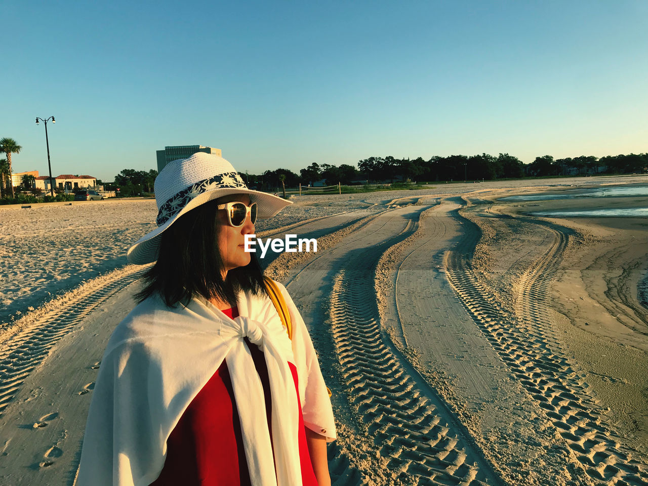 Woman wearing hat while standing at beach against clear blue sky