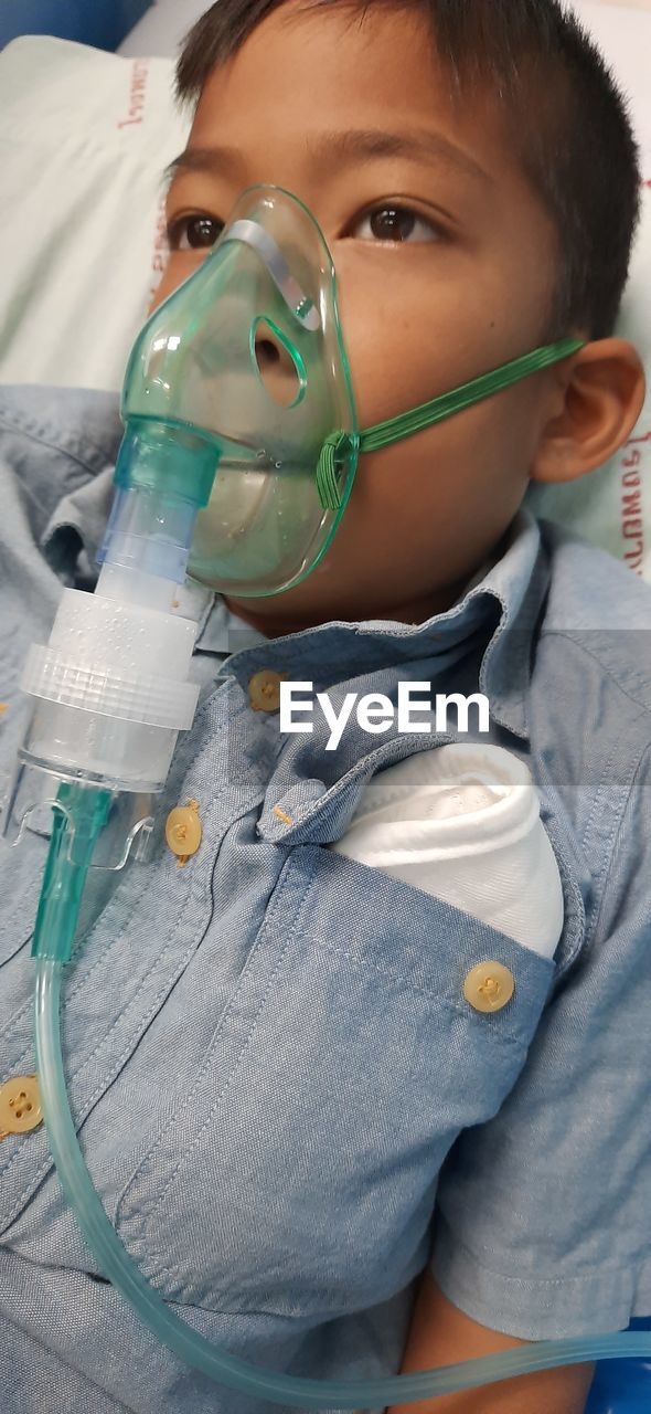 Close-up of boy with oxygen mask lying on bed in hospital