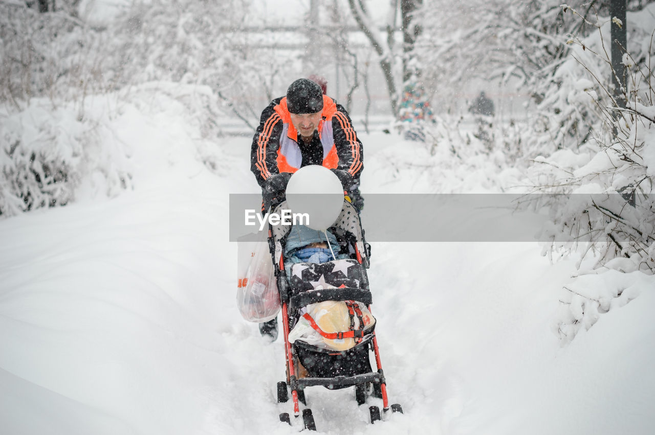 Man pushing baby carriage on snow