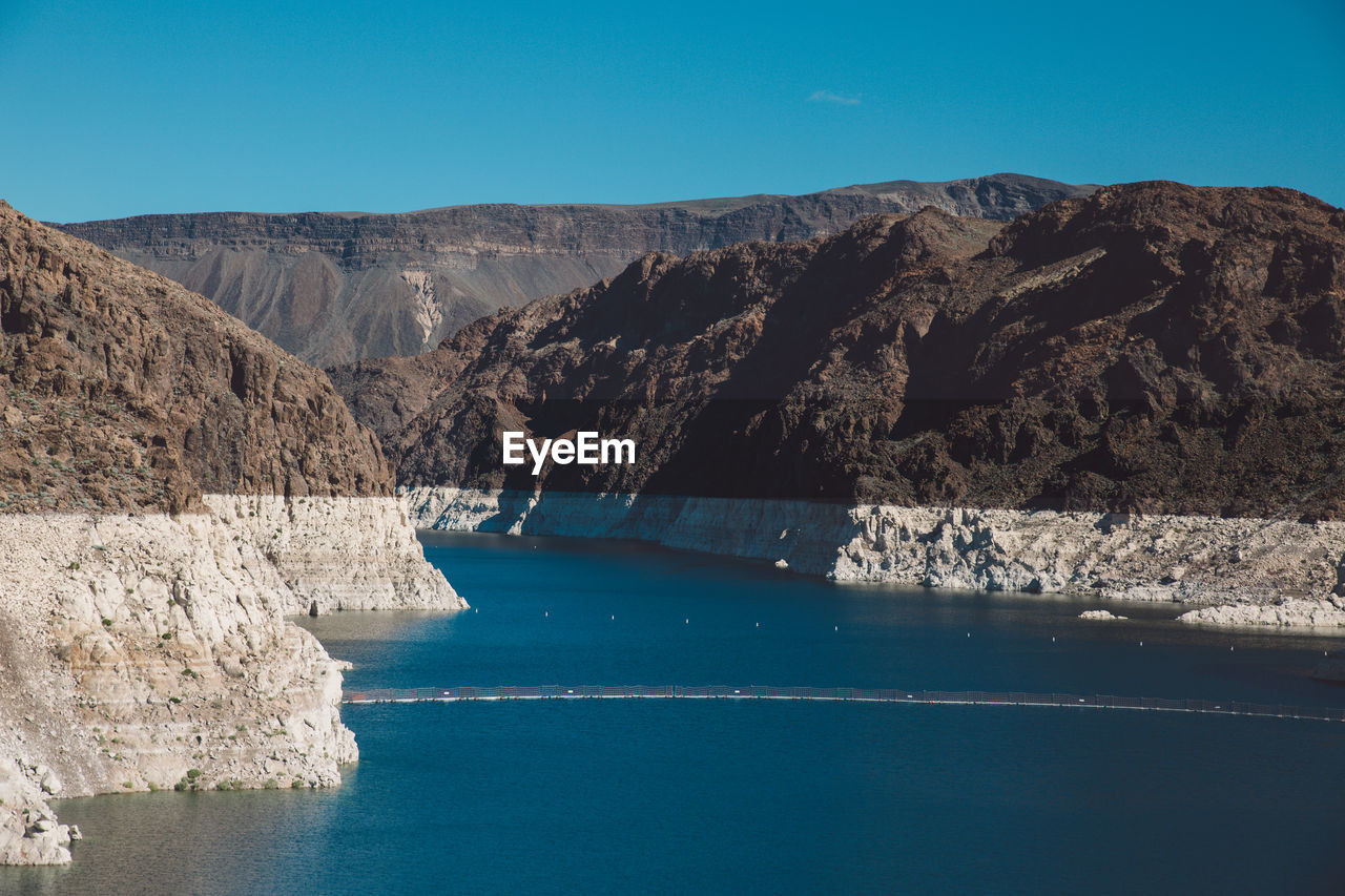 Colorado river amidst mountain at hoover dam against clear blue sky