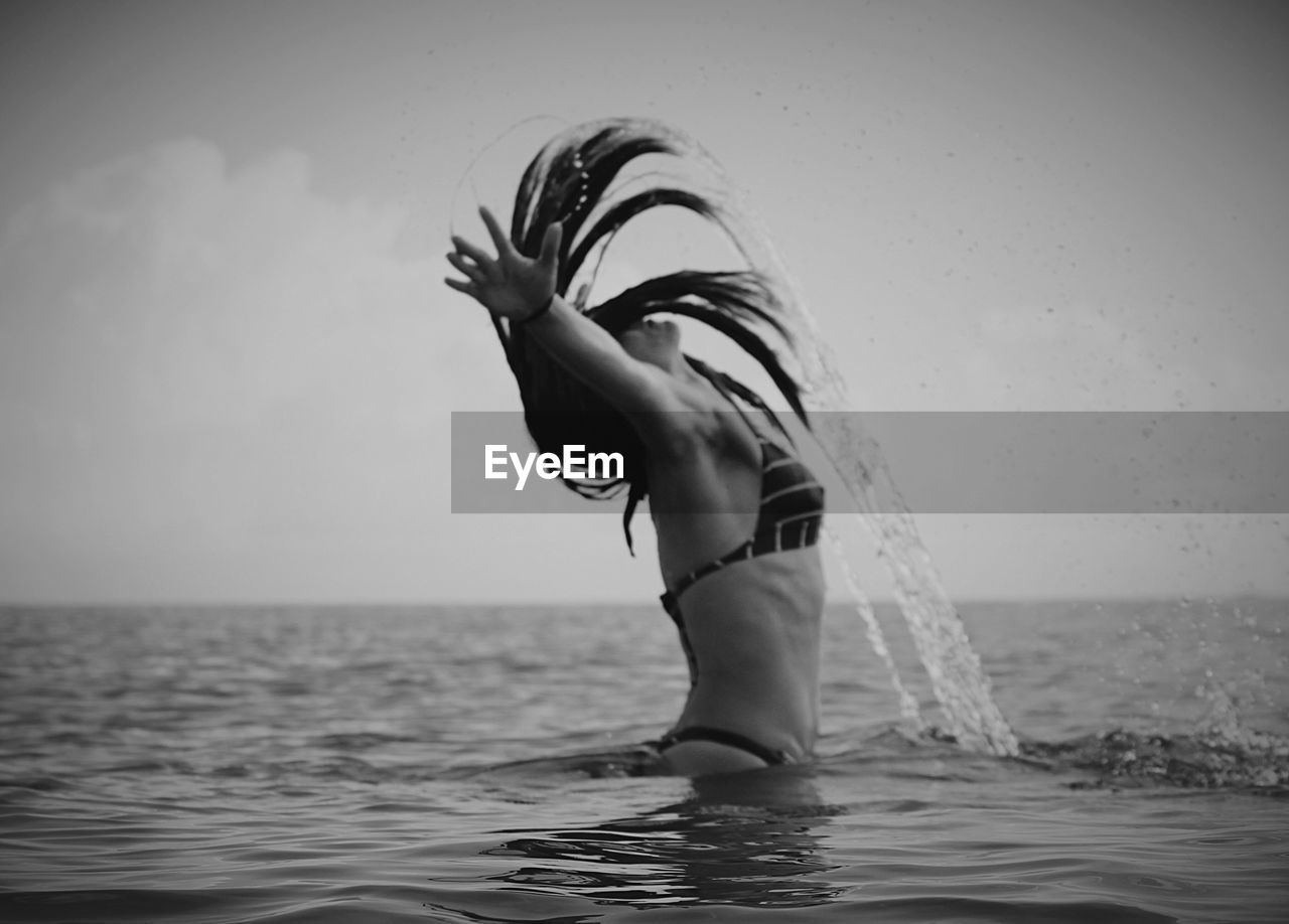 Side view of woman splashing water with hair in sea