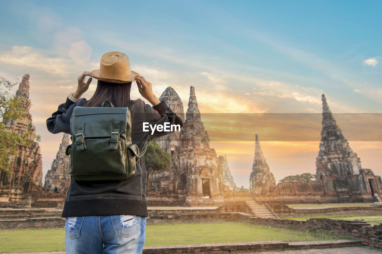 Rear view of woman with backpack standing at temple against sky during sunset