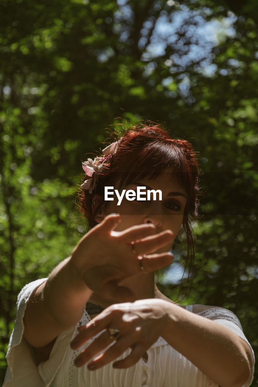 Portrait of young woman gesturing while standing against trees