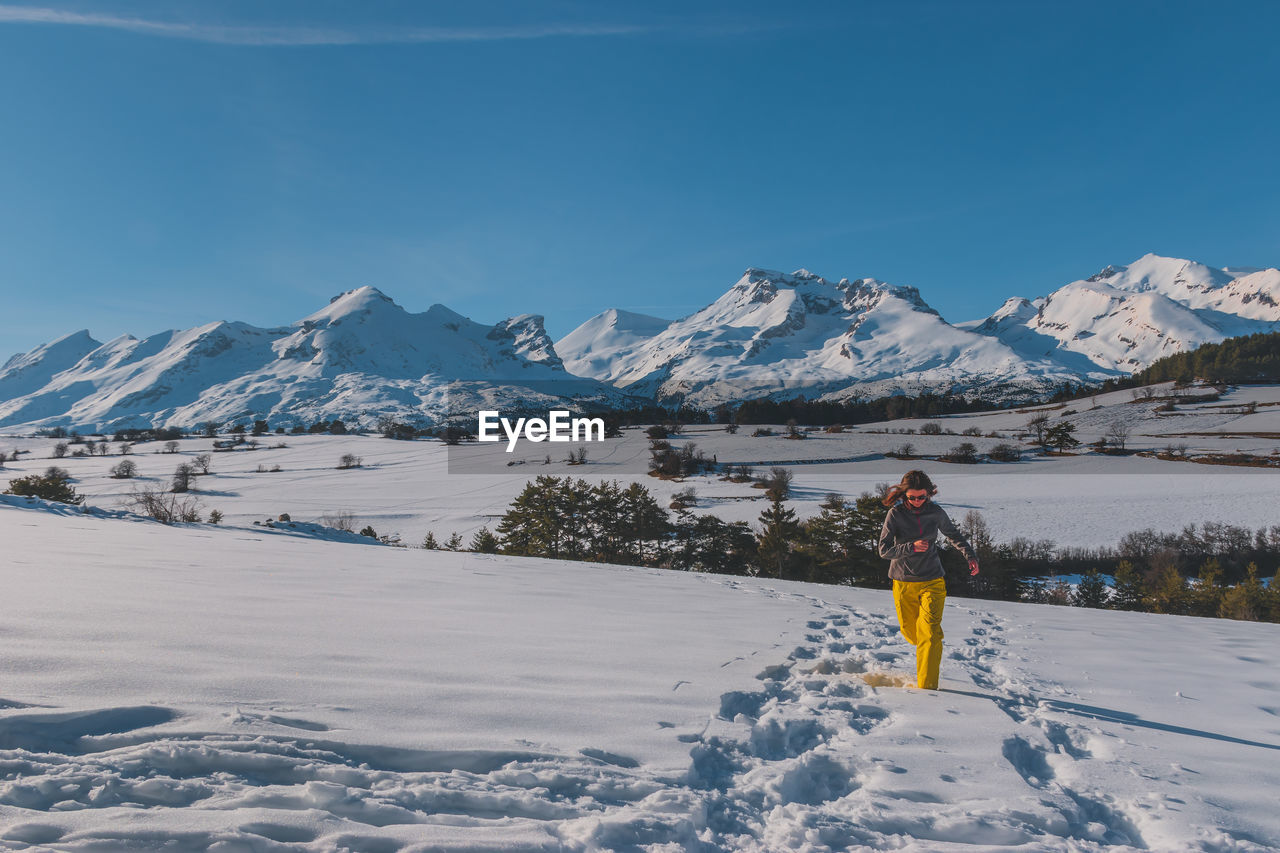 A full-body shot of a young caucasian woman running towards the camera in the french alps mountains