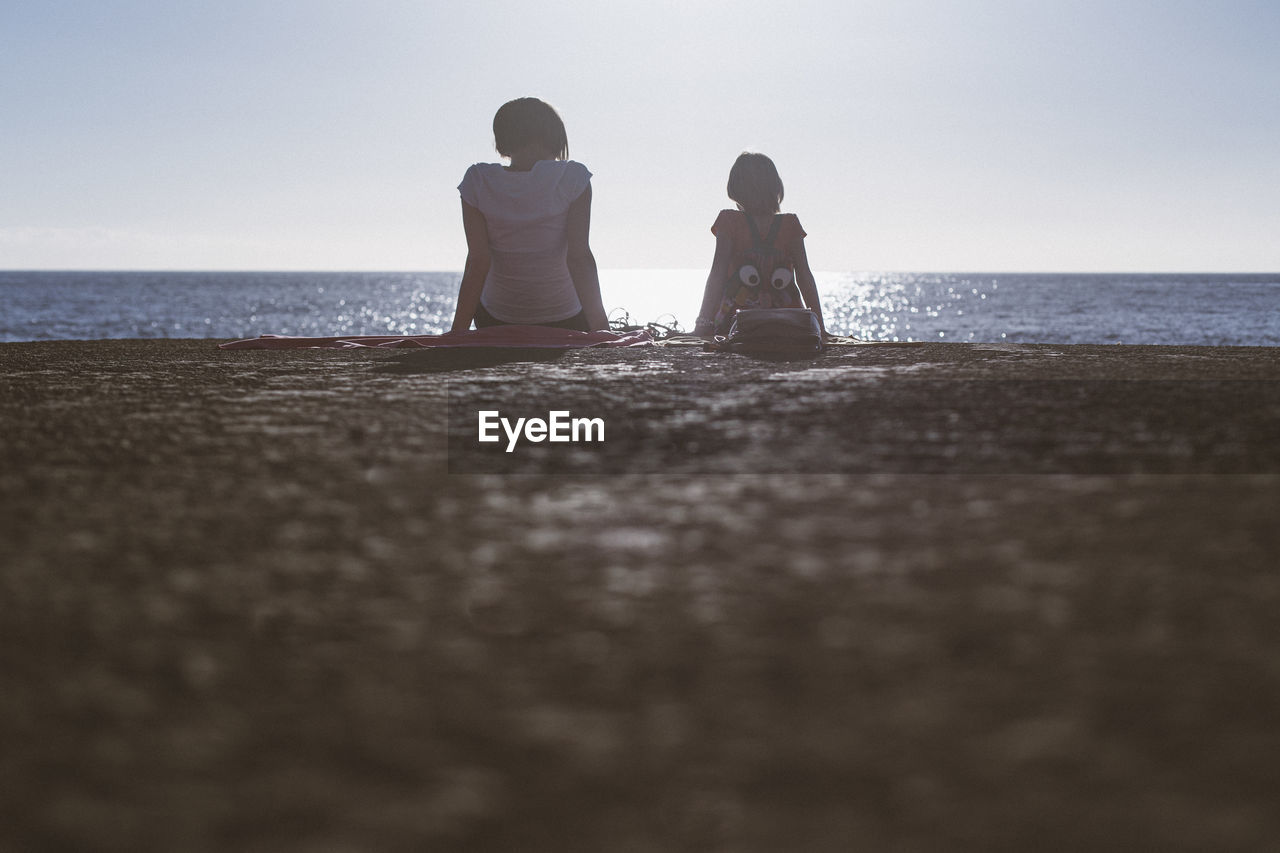 REAR VIEW OF PEOPLE SITTING ON BEACH