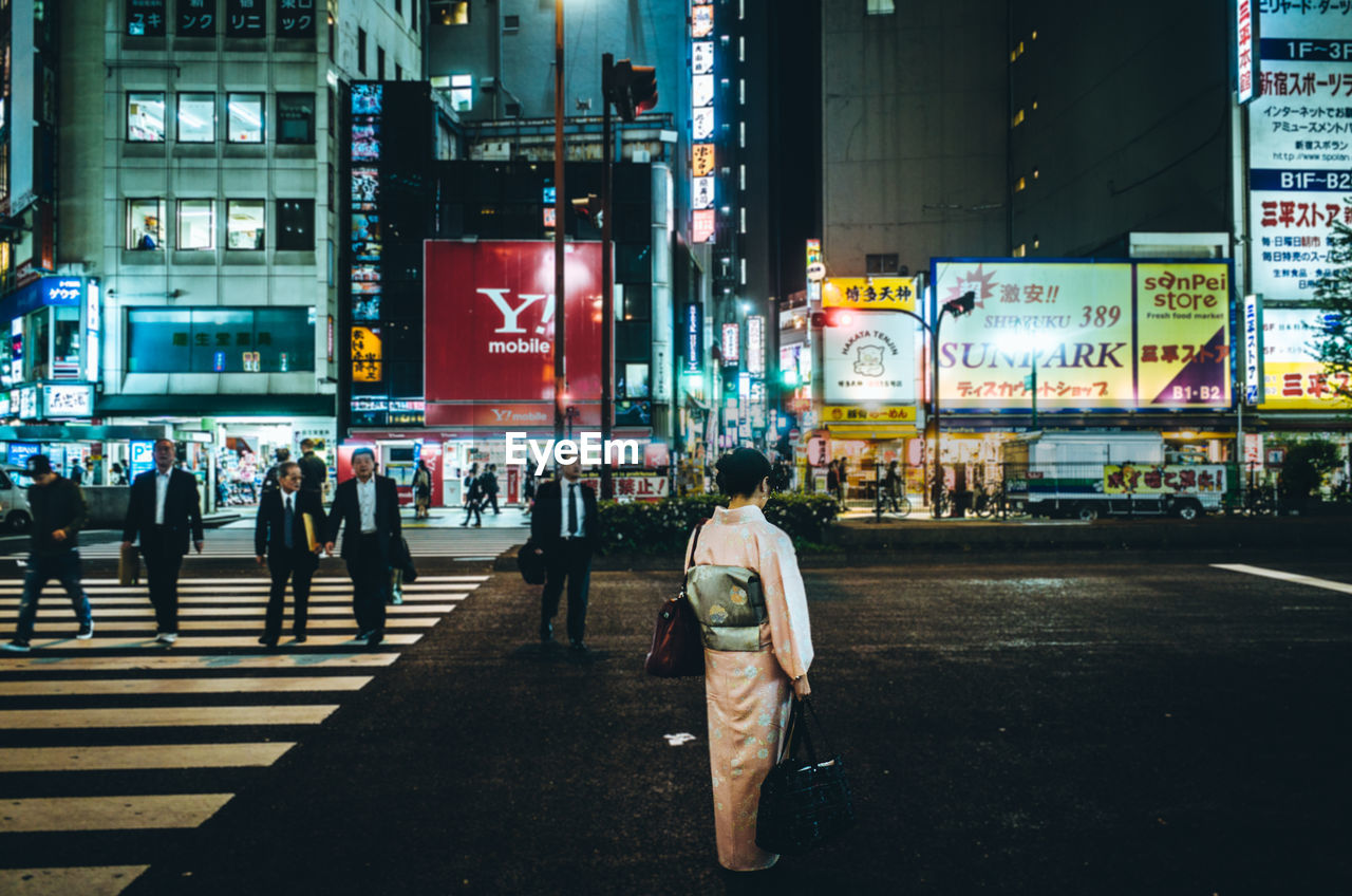 PEOPLE WALKING ON ILLUMINATED ROAD AT NIGHT