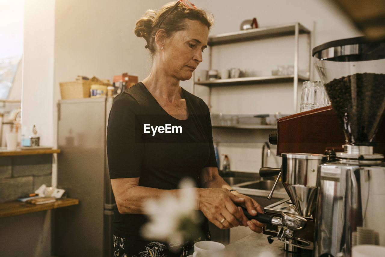 Senior female owner making coffee in cafe
