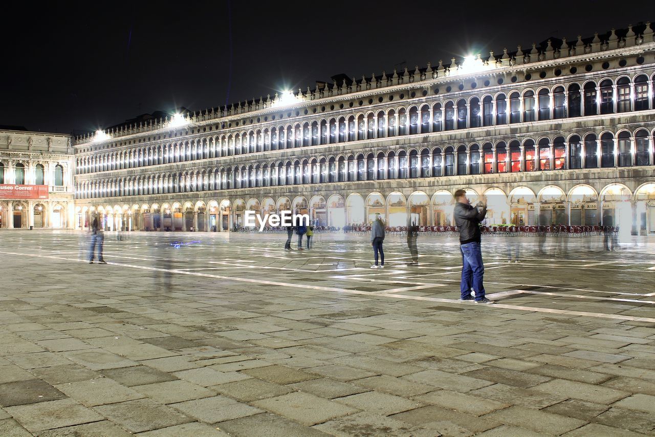 PEOPLE AT ILLUMINATED TOWN SQUARE AGAINST SKY