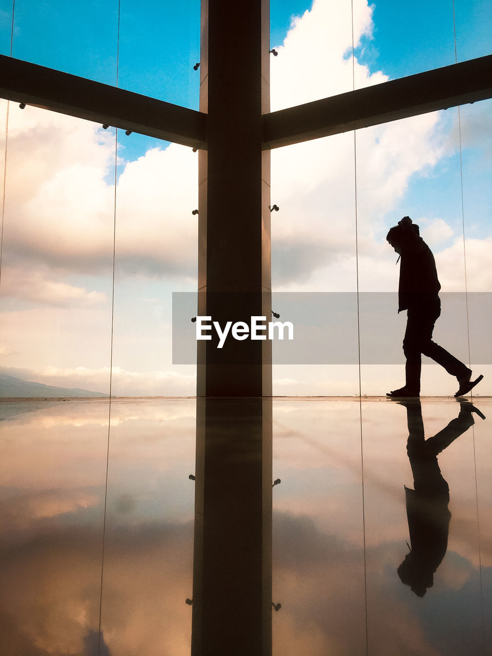 Silhouette man standing by window against sky